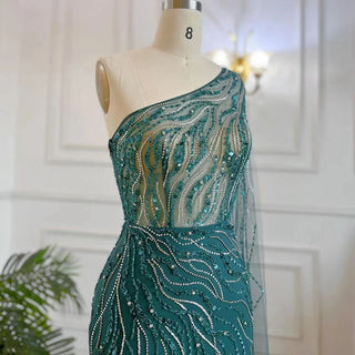 Desert Blossom: One-Shoulder Blush Pink Mermaid Evening Gown with Cape, Accented in Dubai-Inspired Emerald Green - A Luxurious Ensemble for Weddings and Grand Parties.